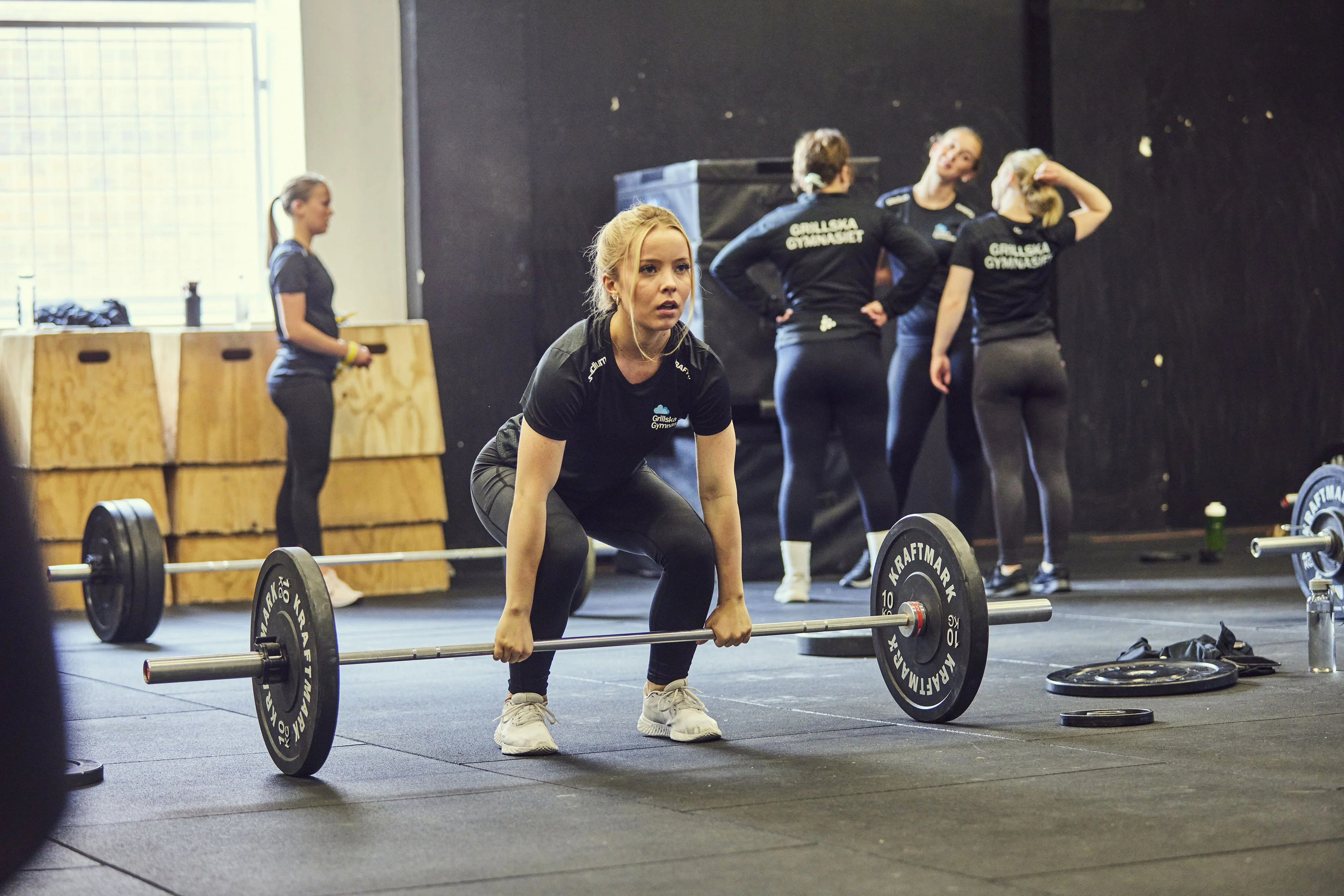 Elev lyfter skivstång i gym med andra elever i bakgrunden, alla i träningskläder från Grillska Gymnasiet.