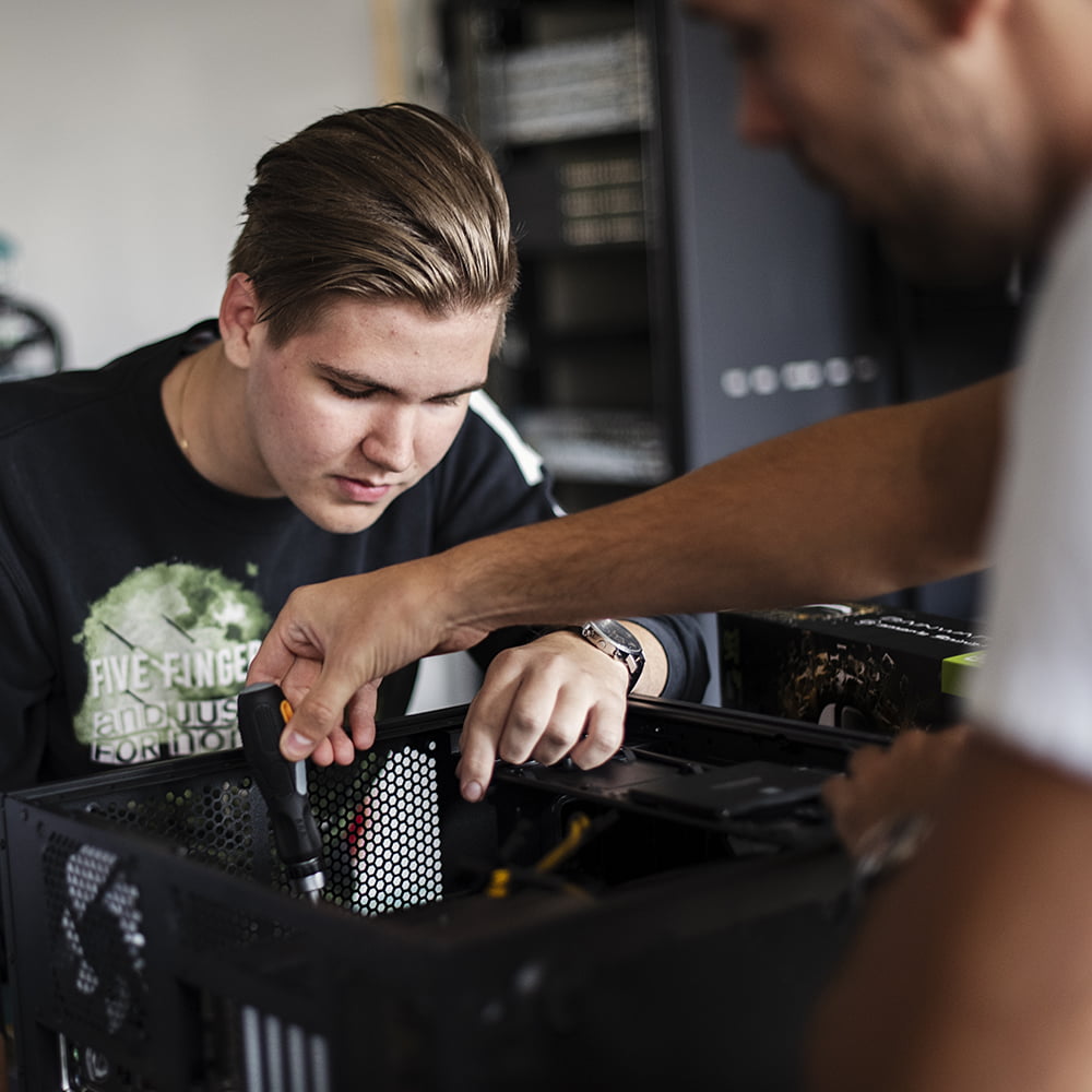 Två elever monterar en dator på El- och Energi&shy;programmet IT. En ung man tittar fokuserat medan den andra personen skruvar i chassit. Servrar syns i bakgrunden.