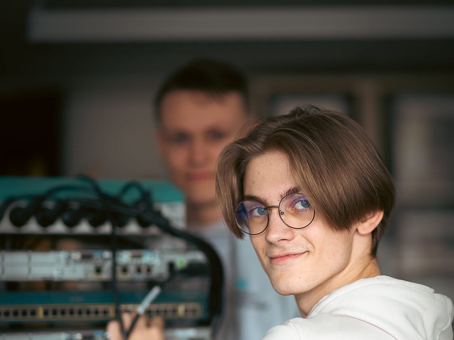 Elev kopplar nätverkskablar i en serverhall och ler mot kameran.