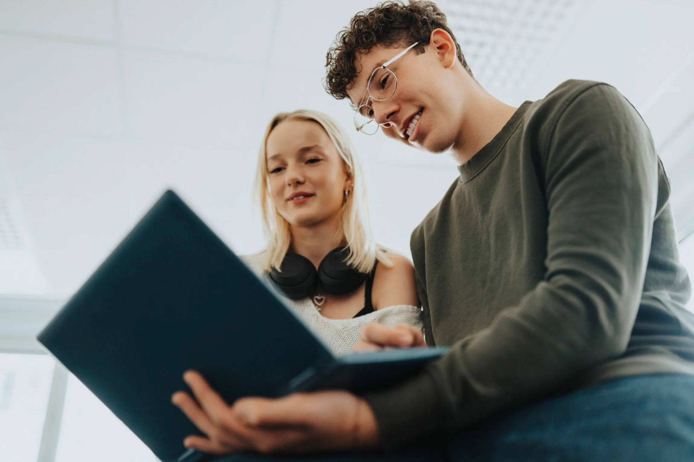 En elev med lockigt hår sitter vid en dator och ler. En annan elev syns suddigt i bakgrunden.