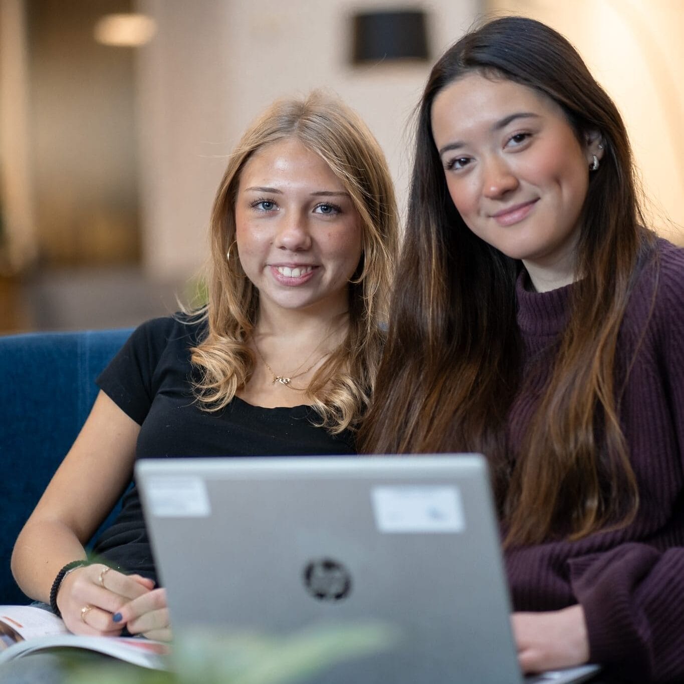 Två unga tjejer som sitter nära varandra och håller i en laptop. 