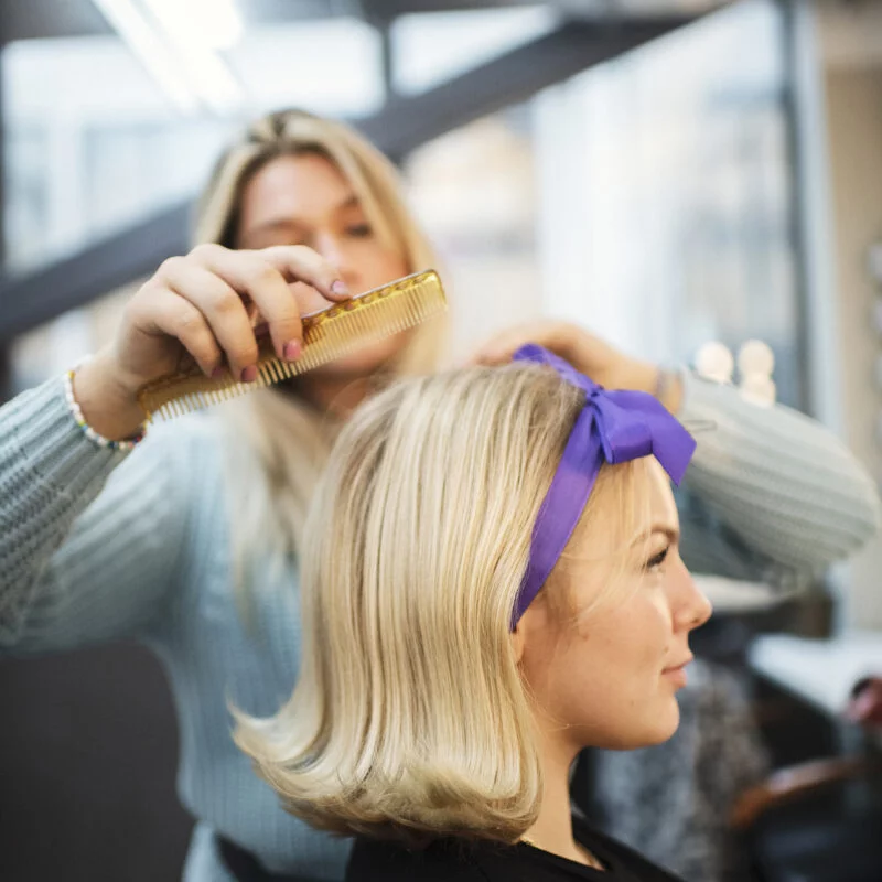 Frisörelev kammar håret på en kund med en lila rosett.