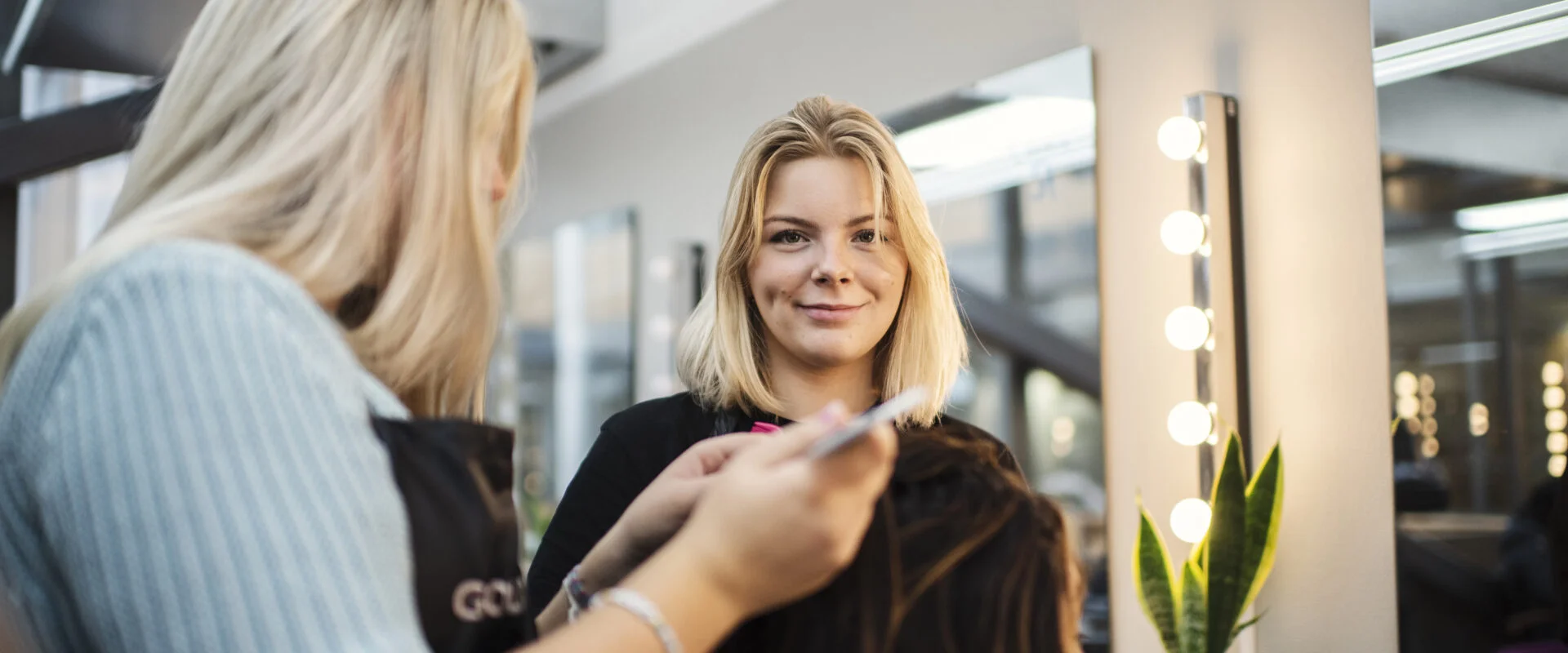 Två elever på frisörlinjen fixar med en kunds hår
