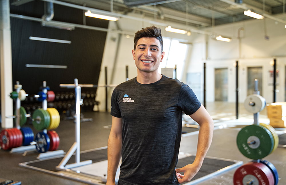 En glad elev från samhällsvetenskapsprogrammet beteende som står inuti ett gym.
