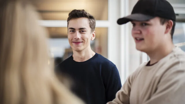 Två elever på teknikprogrammet samtalar i en skolmiljö, en av dem ler mot kameran.