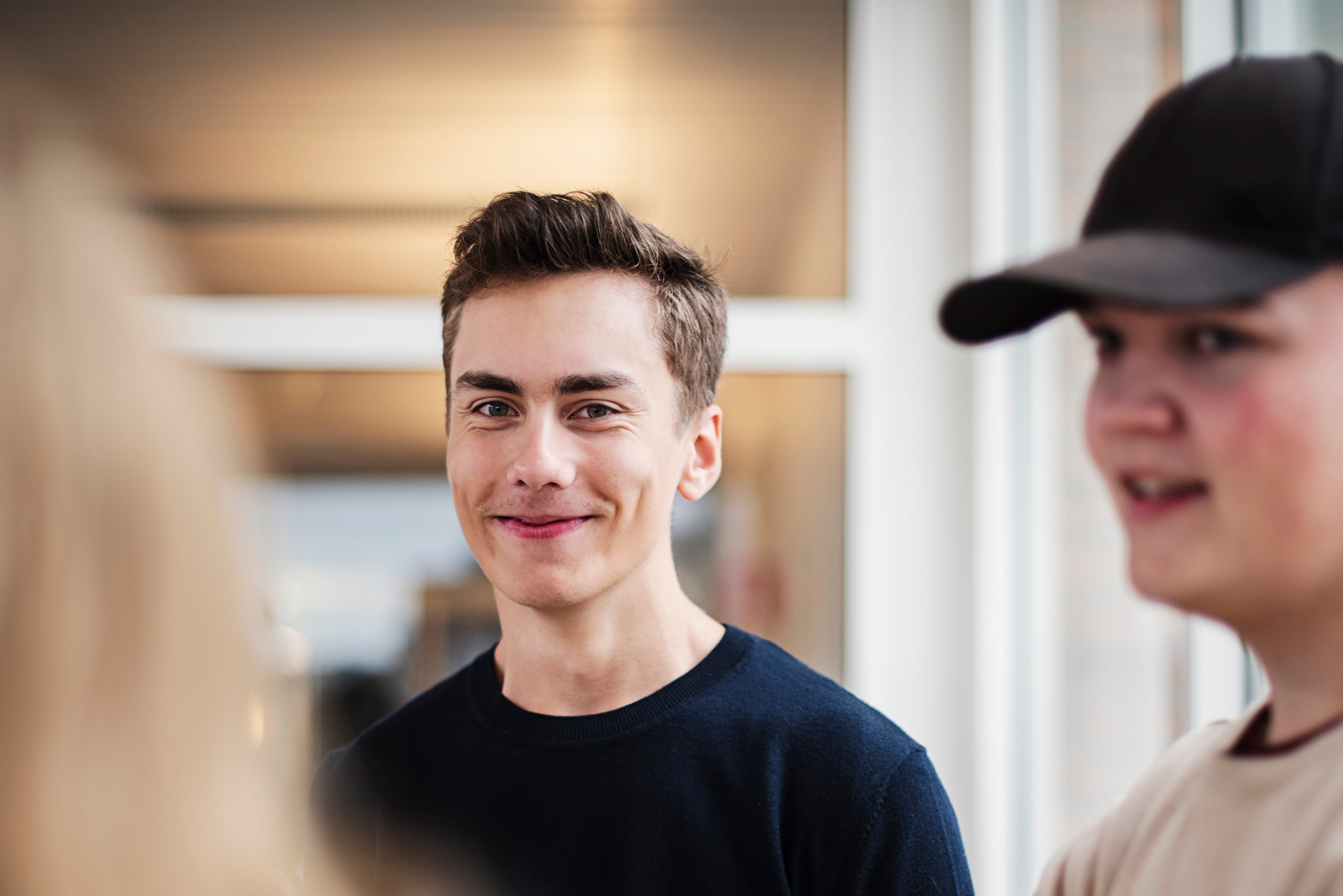 Två elever på teknik&shy;programmet samtalar i en skolmiljö, en av dem ler mot kameran.