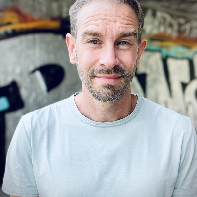 Lärare Jonny Nilsson står framför en vägg med graffiti. Han ser rakt in i kameran och ler.